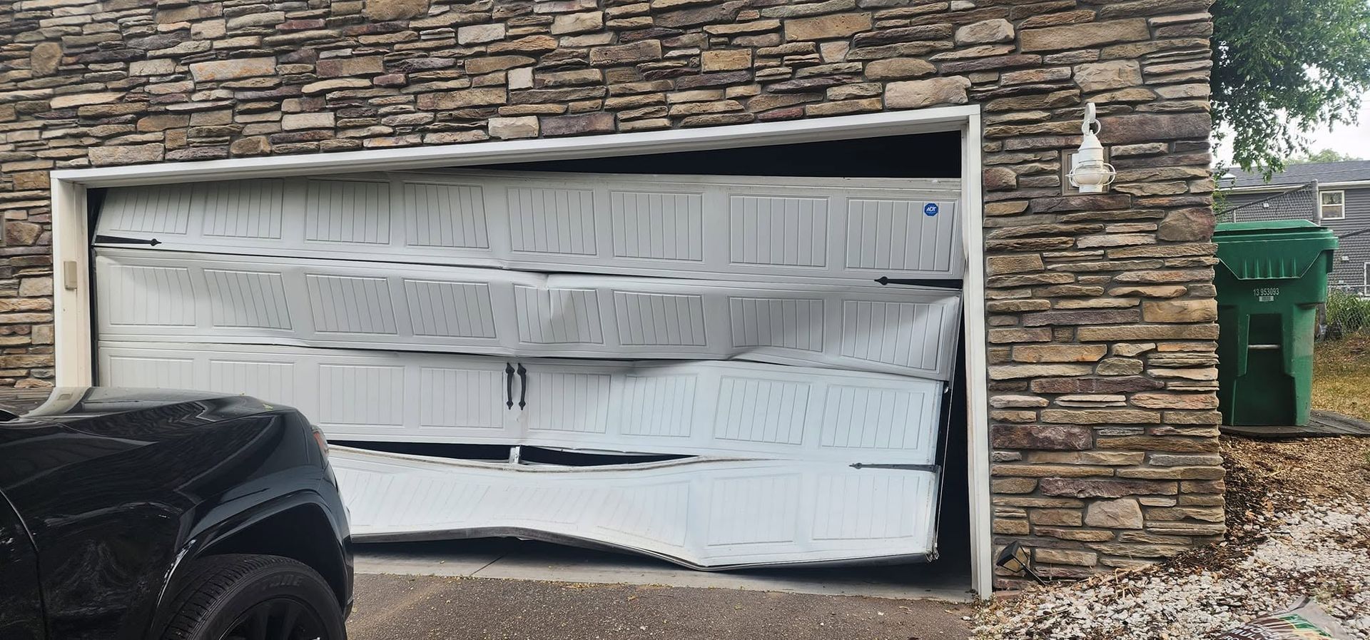 Collapsed white garage door on a stone house, with a car parked in front.