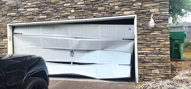 Collapsed white garage door on a stone house, with a car parked in front.