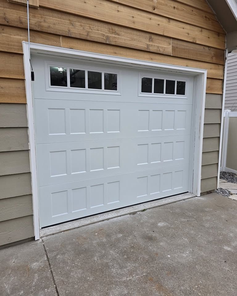 White garage door with small windows in a tan-sided house, viewed from the driveway