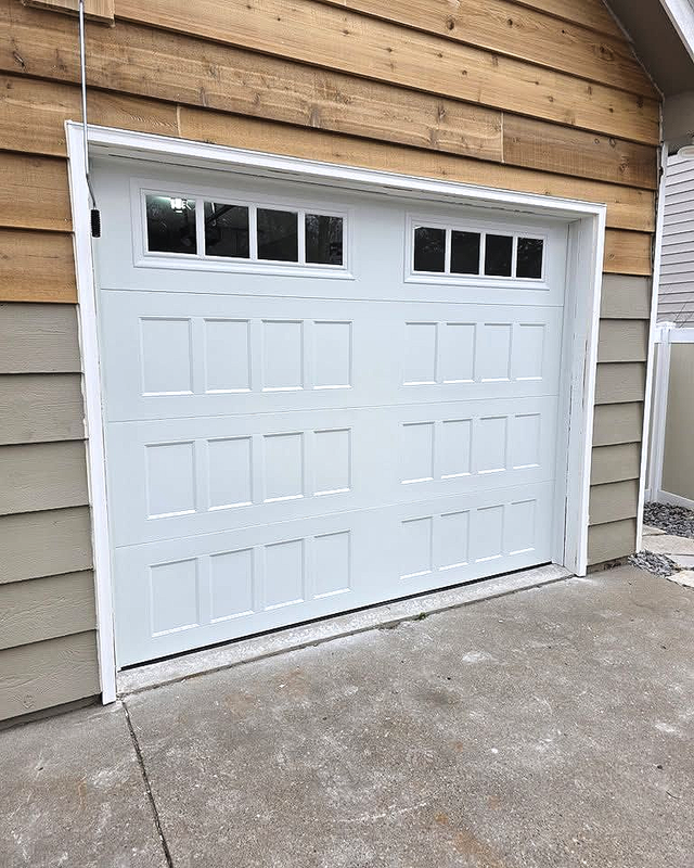 White garage door with small windows in a tan-sided house, viewed from the driveway