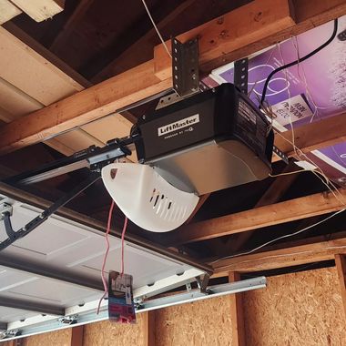 Garage ceiling with a mounted garage door opener, tracks, and exposed wooden beams.