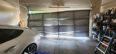 Garage interior with a silver car, closed sectional door, and shelves of stored items on the right