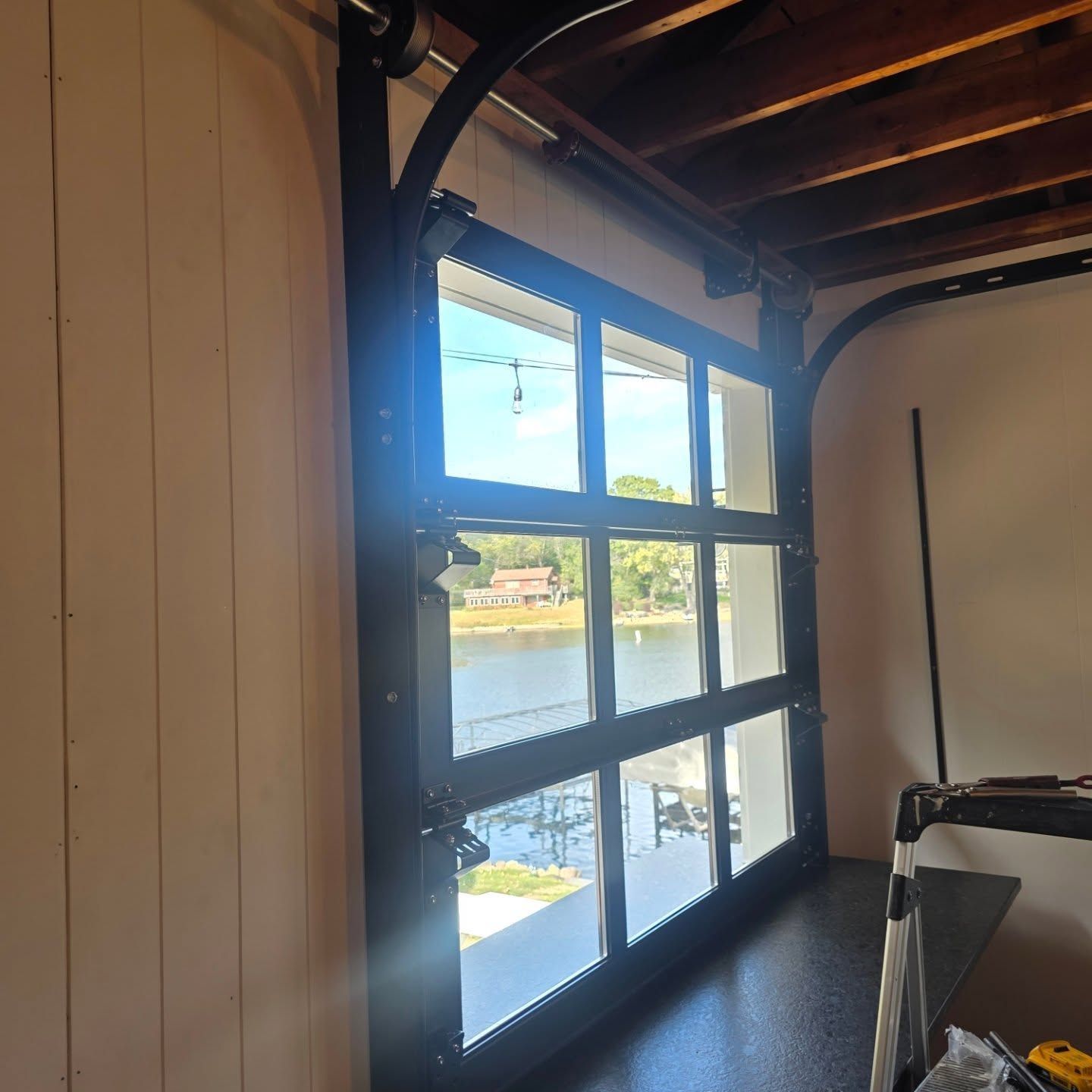 Wood-framed window overlooking a river, with sunlight and a wooden interior ceiling visible.