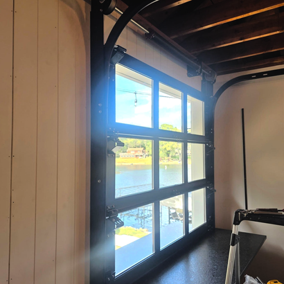 Wood-framed window overlooking a river, with sunlight and a wooden interior ceiling visible.