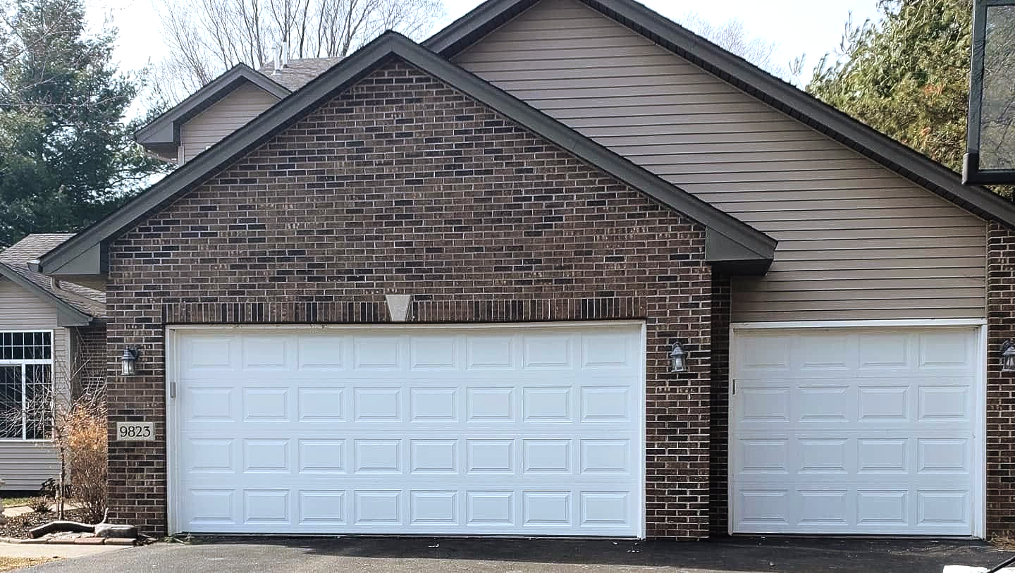 Brick house with two white garage doors and beige siding