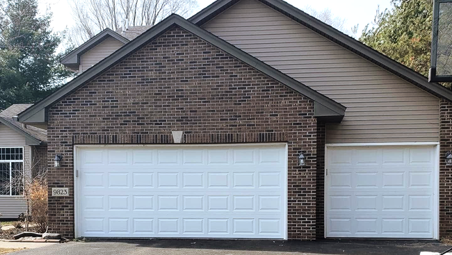 Brick house with two white garage doors and beige siding