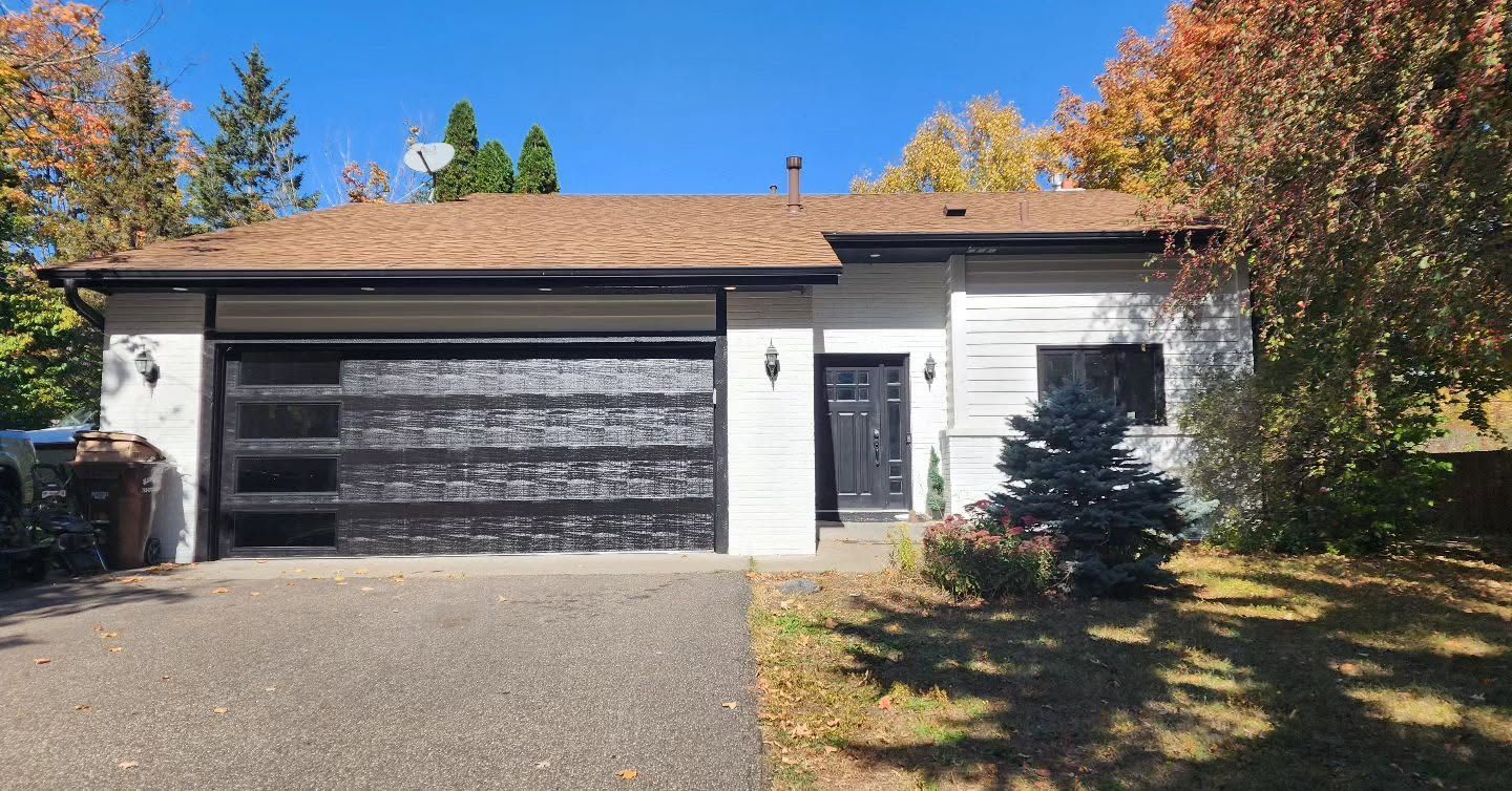 Suburban house with a two-car garage, white siding, black door, and fall trees in the yard
