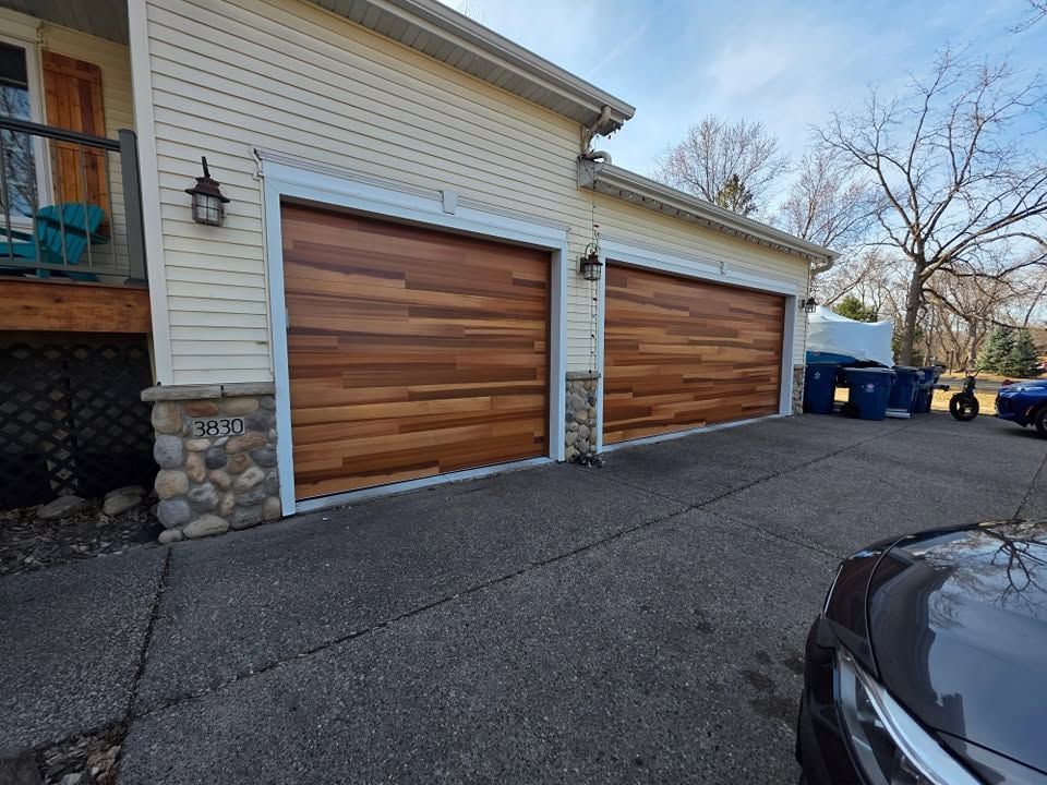 Two wood garage doors on a beige house with a stone trim and driveway
