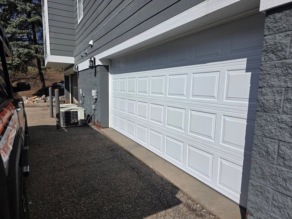 White double garage door beside gray house and gravel driveway with small air-conditioning units