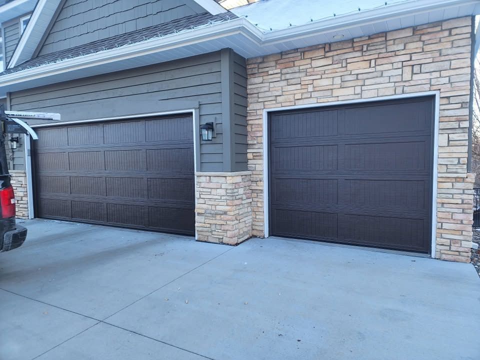 Two dark garage doors on a stone-and-siding house with a concrete driveway.