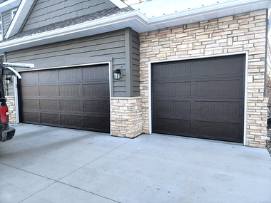 Two adjacent garage doors on a suburban house with stone and gray siding, viewed from the driveway