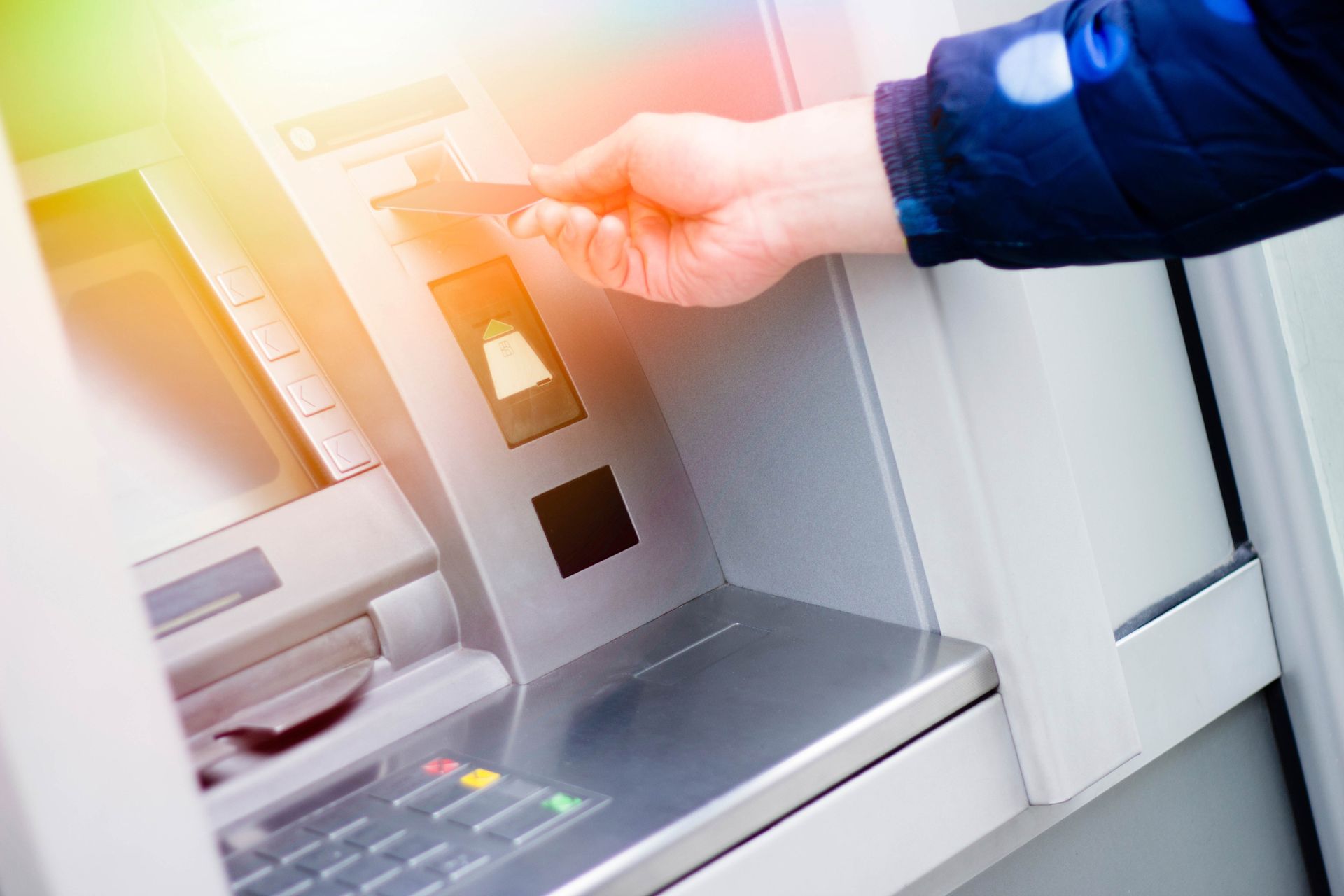 Hand inserting a card into an ATM keypad slot under bright light