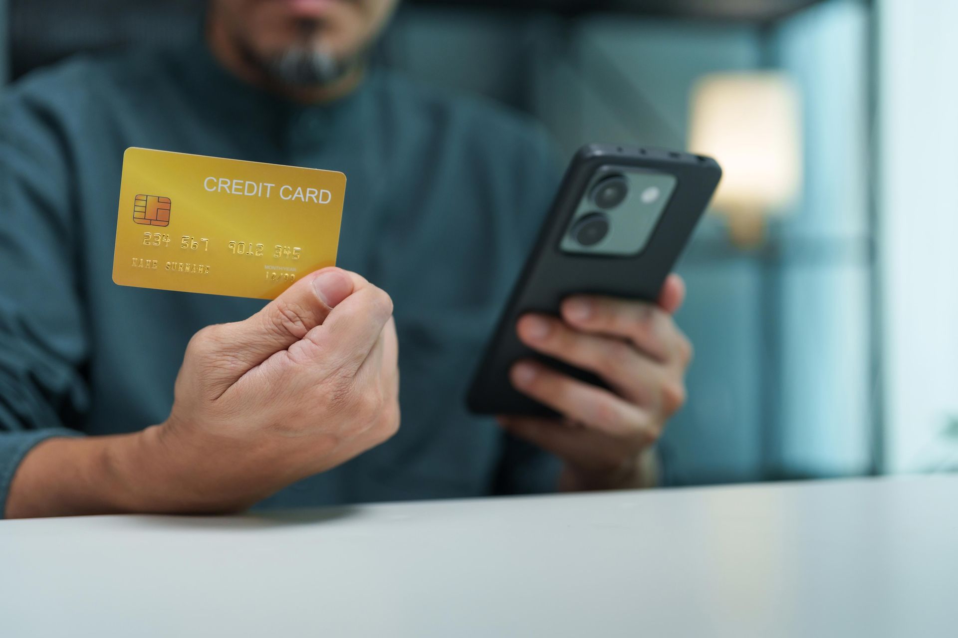 Person holding a yellow credit card and smartphone at a table, suggesting online payment.