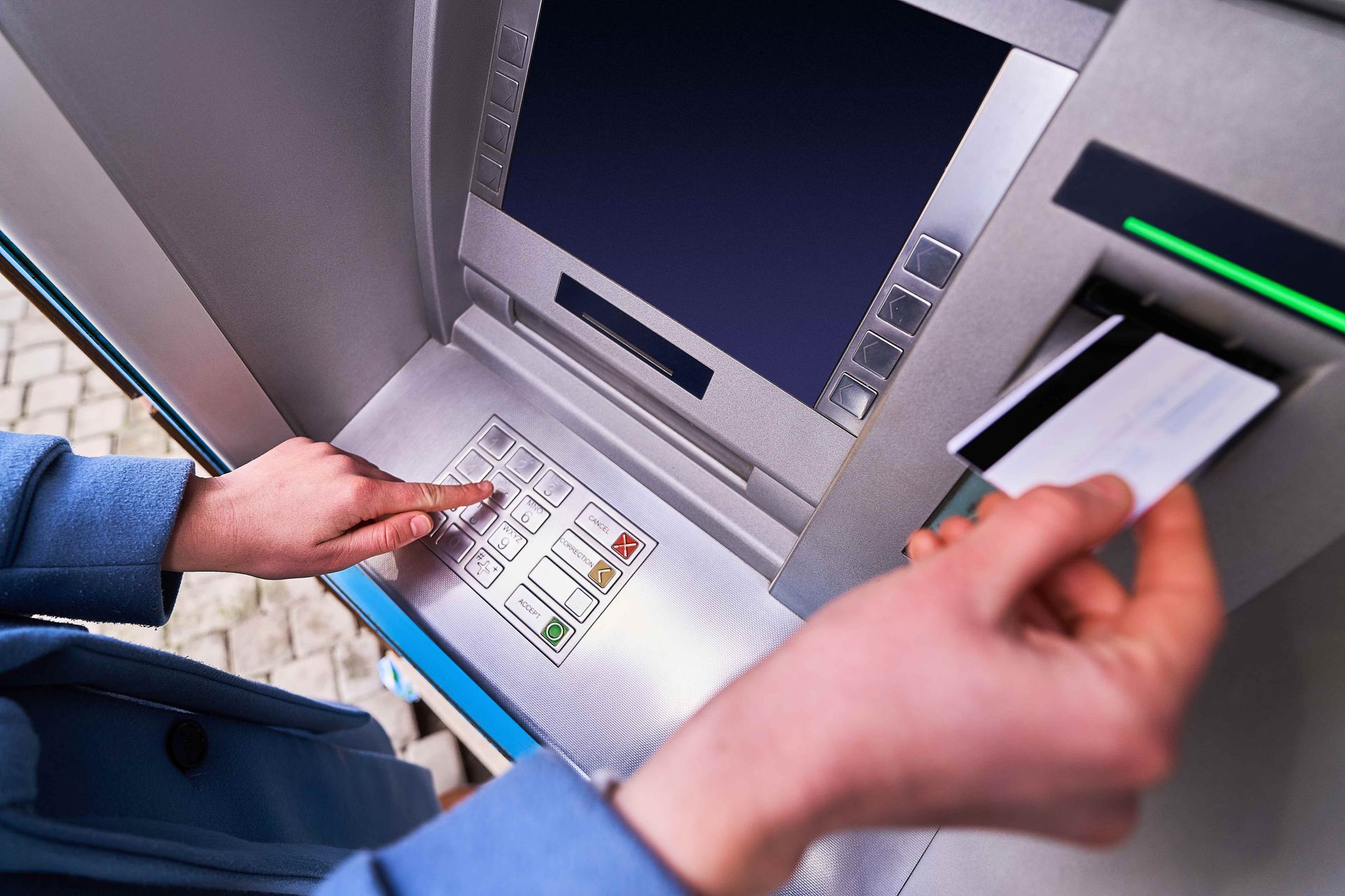 Hands using an ATM, with one hand inserting a card and the screen above showing a transaction menu