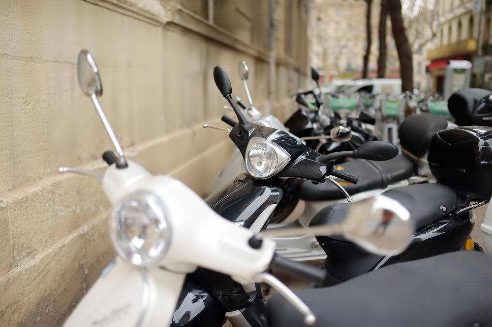 Row of scooters parked along a beige building. White and black scooters with silver mirrors.