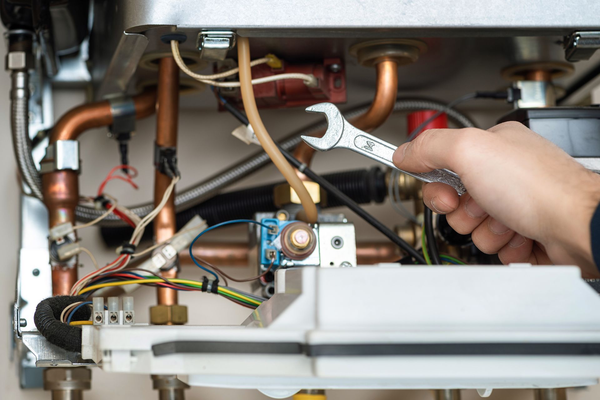 HVAC technician holding a wrench while performing heating repair on boiler system in Etna, Ohio.