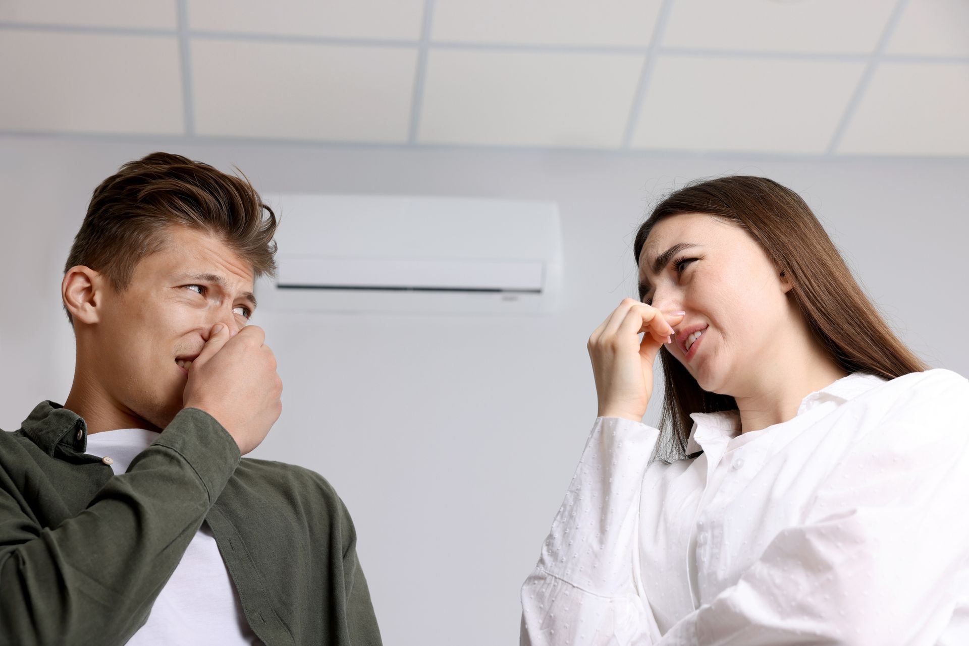 Homeowners covering their noses near an air vent due to a musty smell coming from air conditioning.