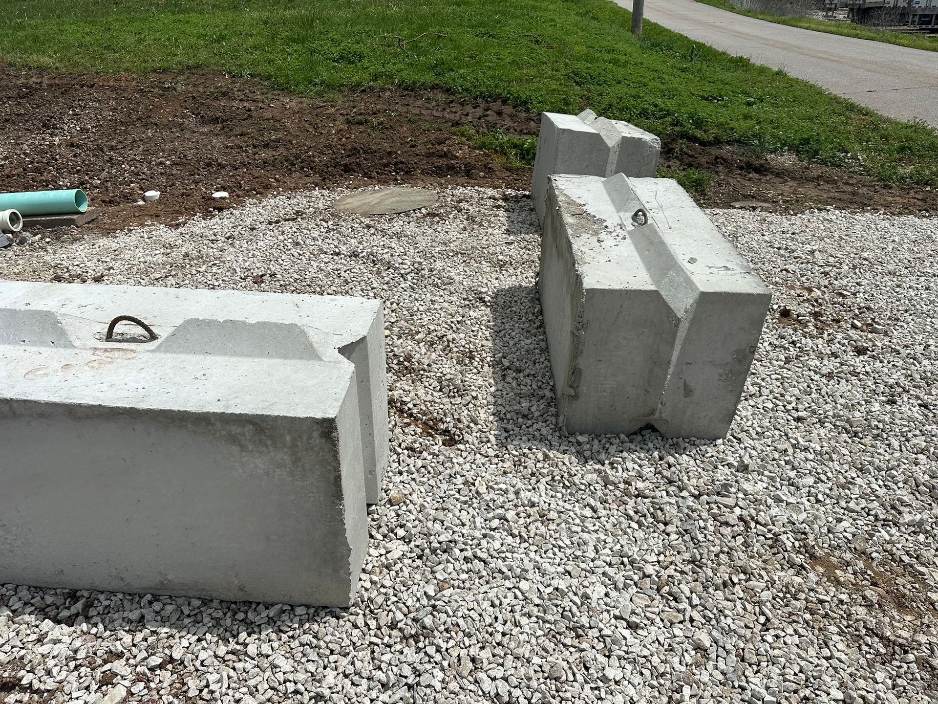 Concrete blocks stacked on gravel beside a grassy roadside verge