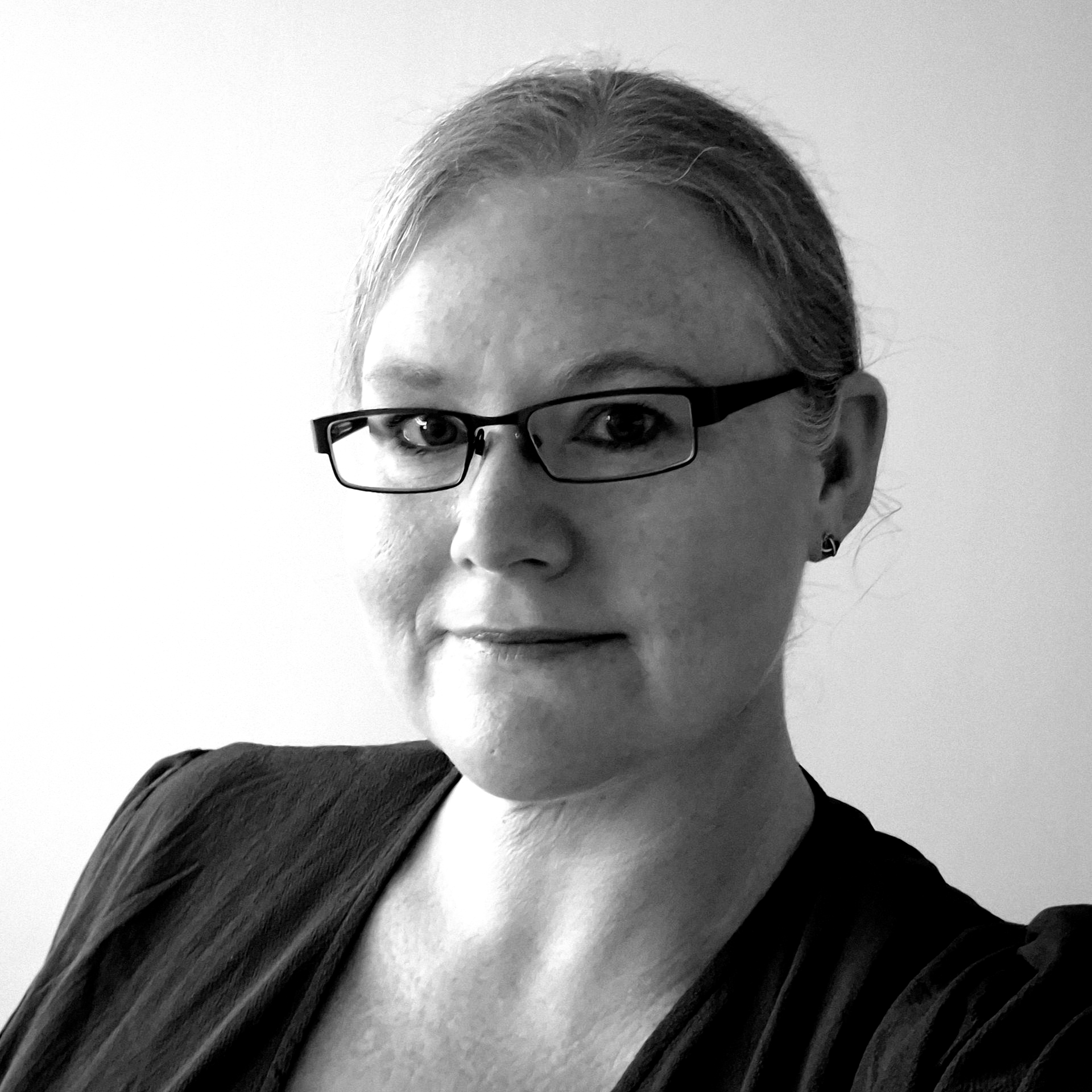 Black-and-white portrait of a person wearing glasses and a dark top, facing the camera with a slight smile