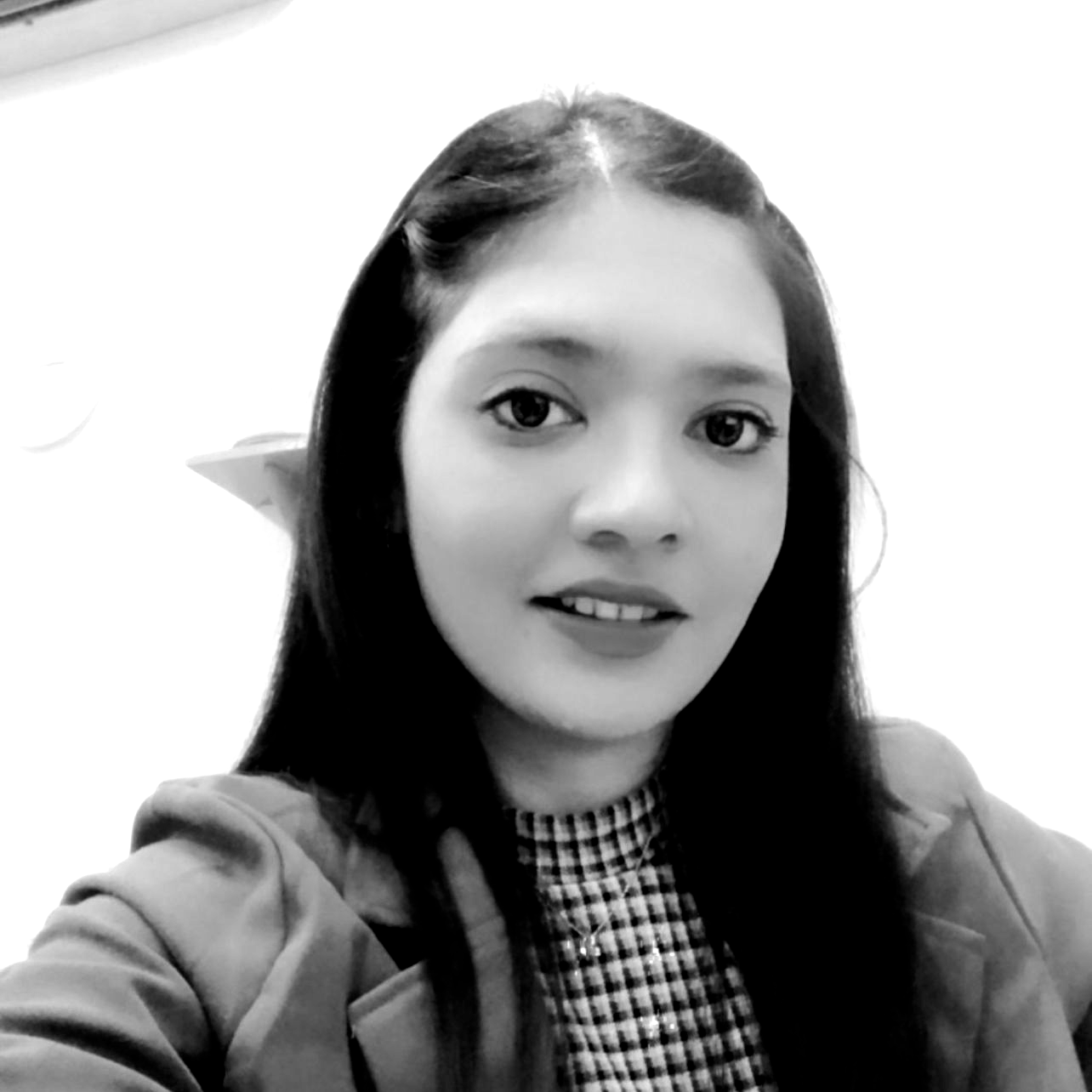 Black-and-white selfie of a smiling person with long dark hair in a checkered top and blazer