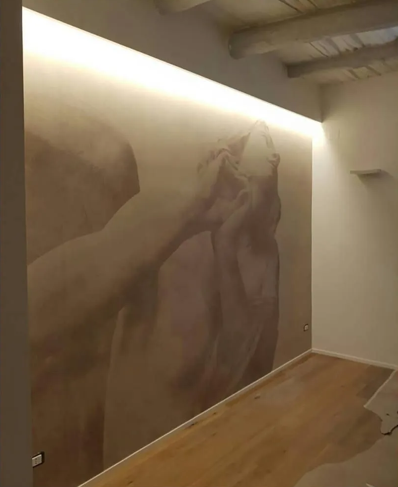 Grande murale raffigurante una mano che tiene un gatto in uno stretto corridoio con pavimento in legno e illuminazione a parete.