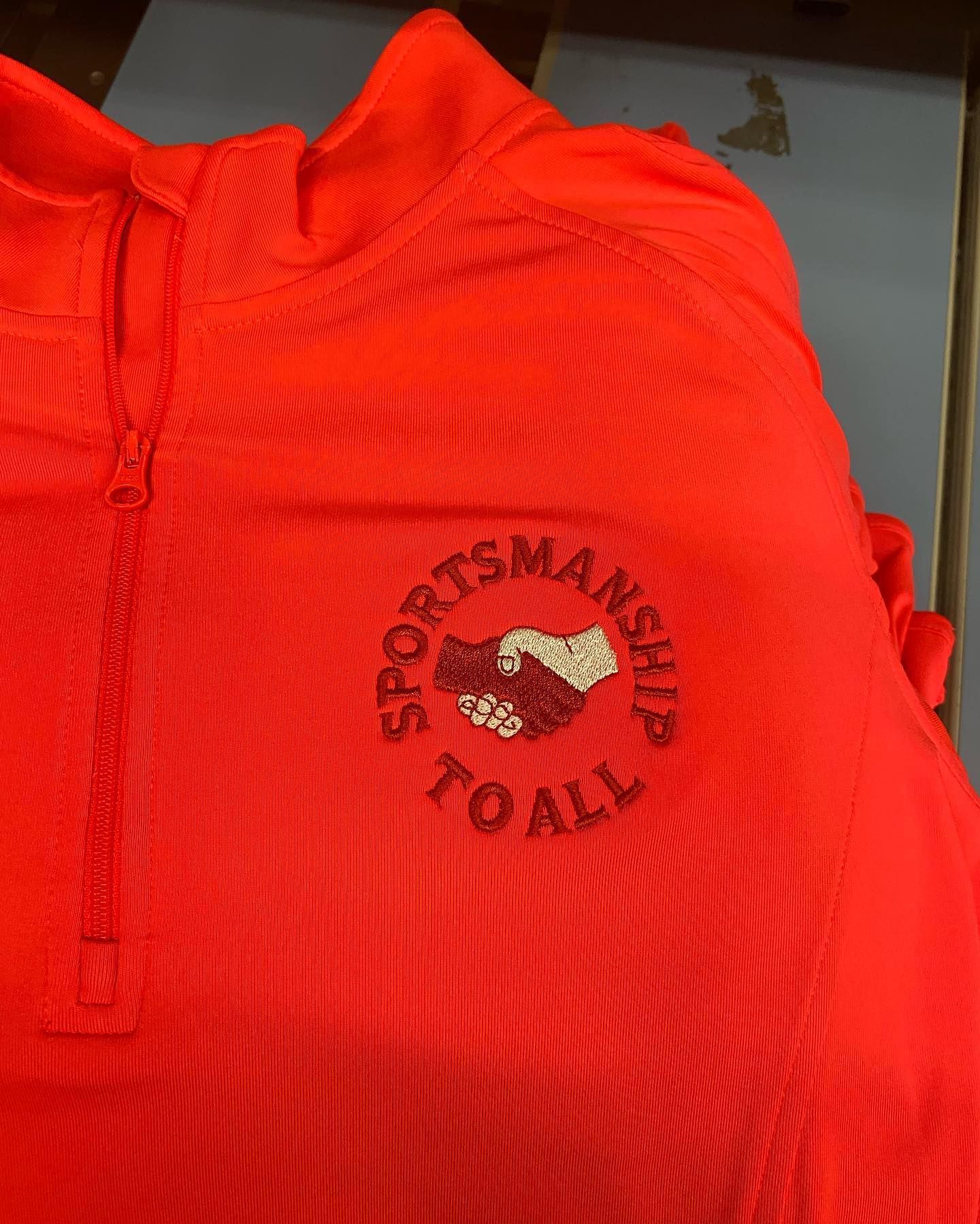 Bright orange quarter-zip shirt with embroidered logo reading