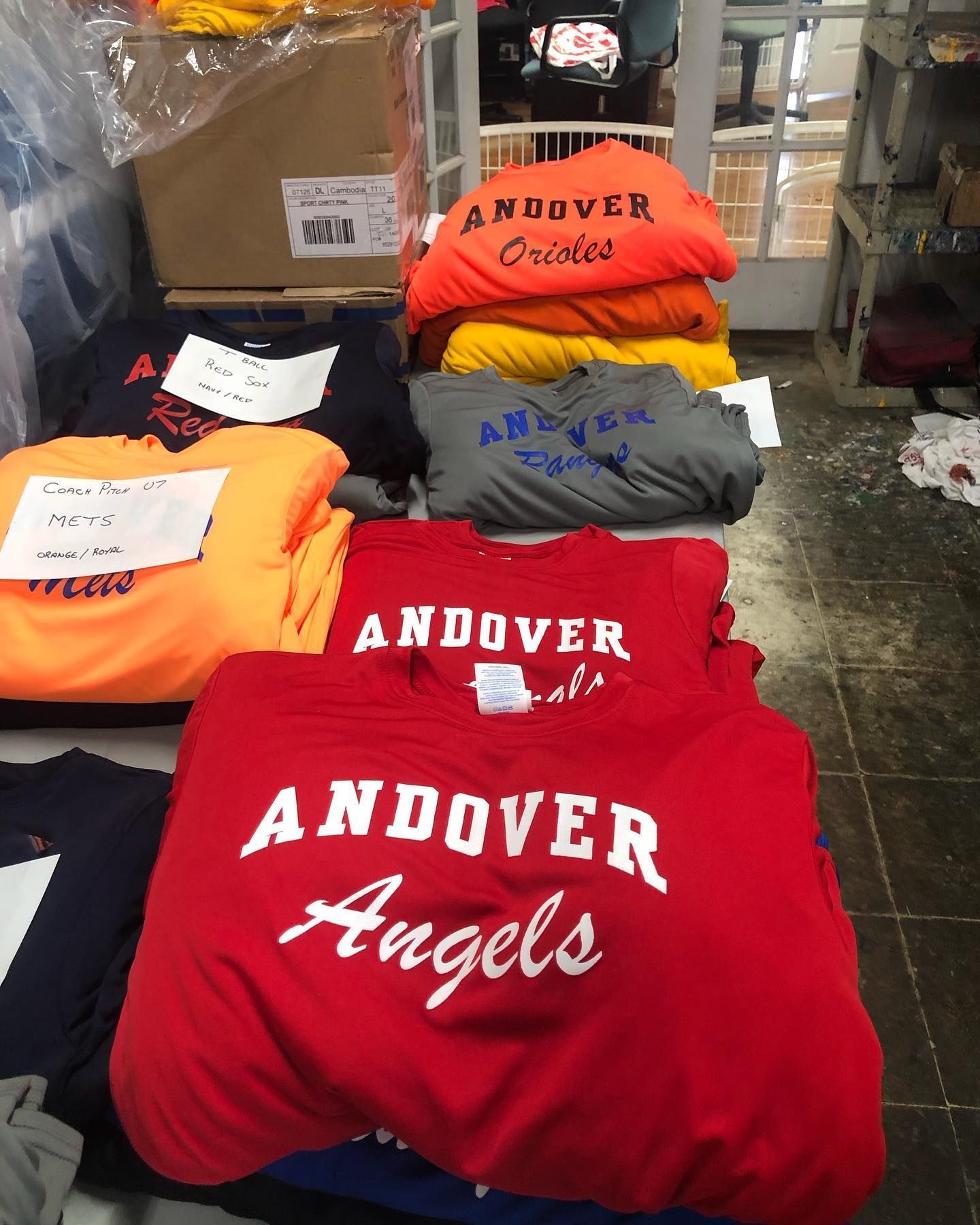 Stacks of Andover spirit wear t-shirts in various colors: red, orange, grey, and navy.