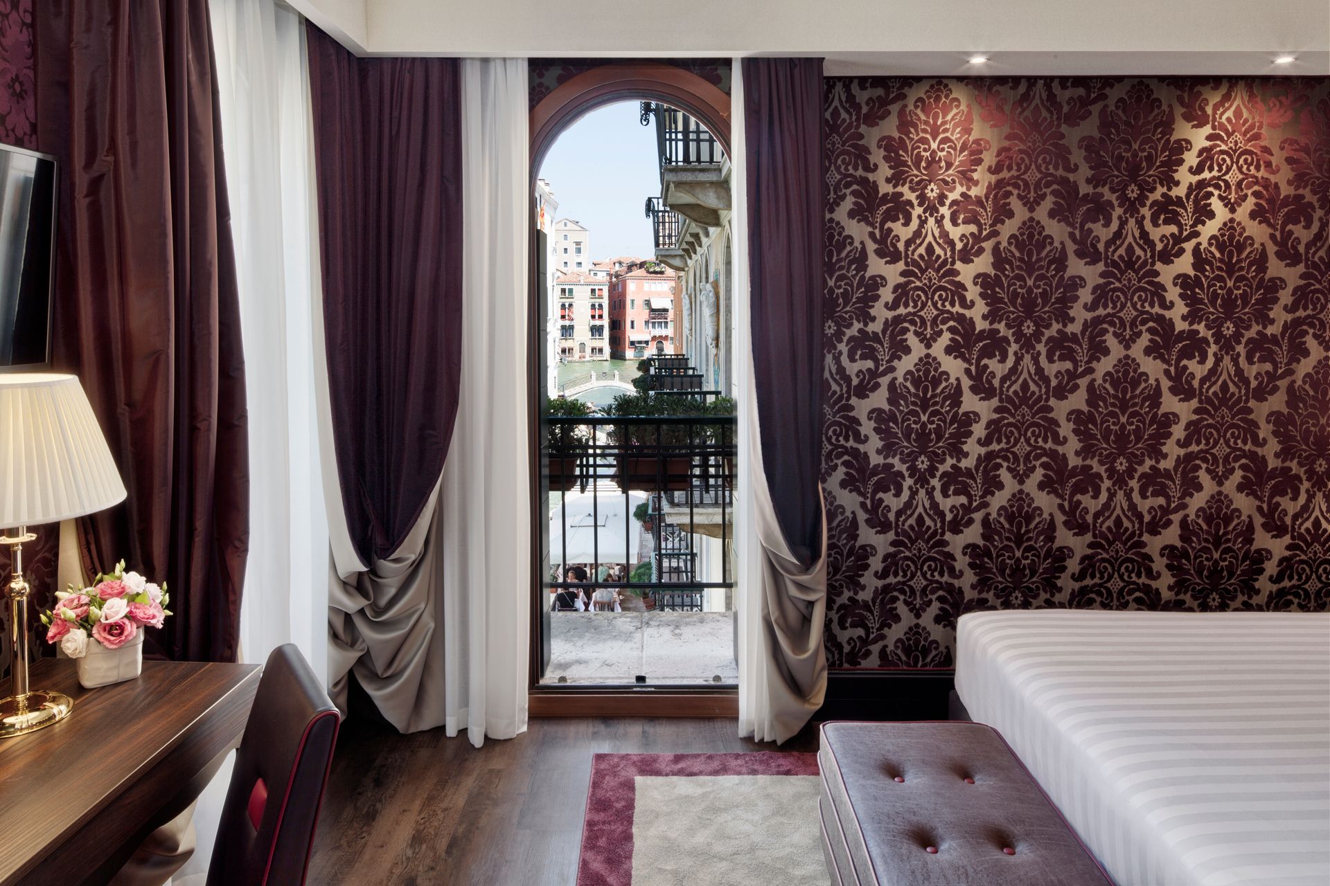 Camera d'albergo con letto, porte finestre e decorazioni murali con motivi viola.