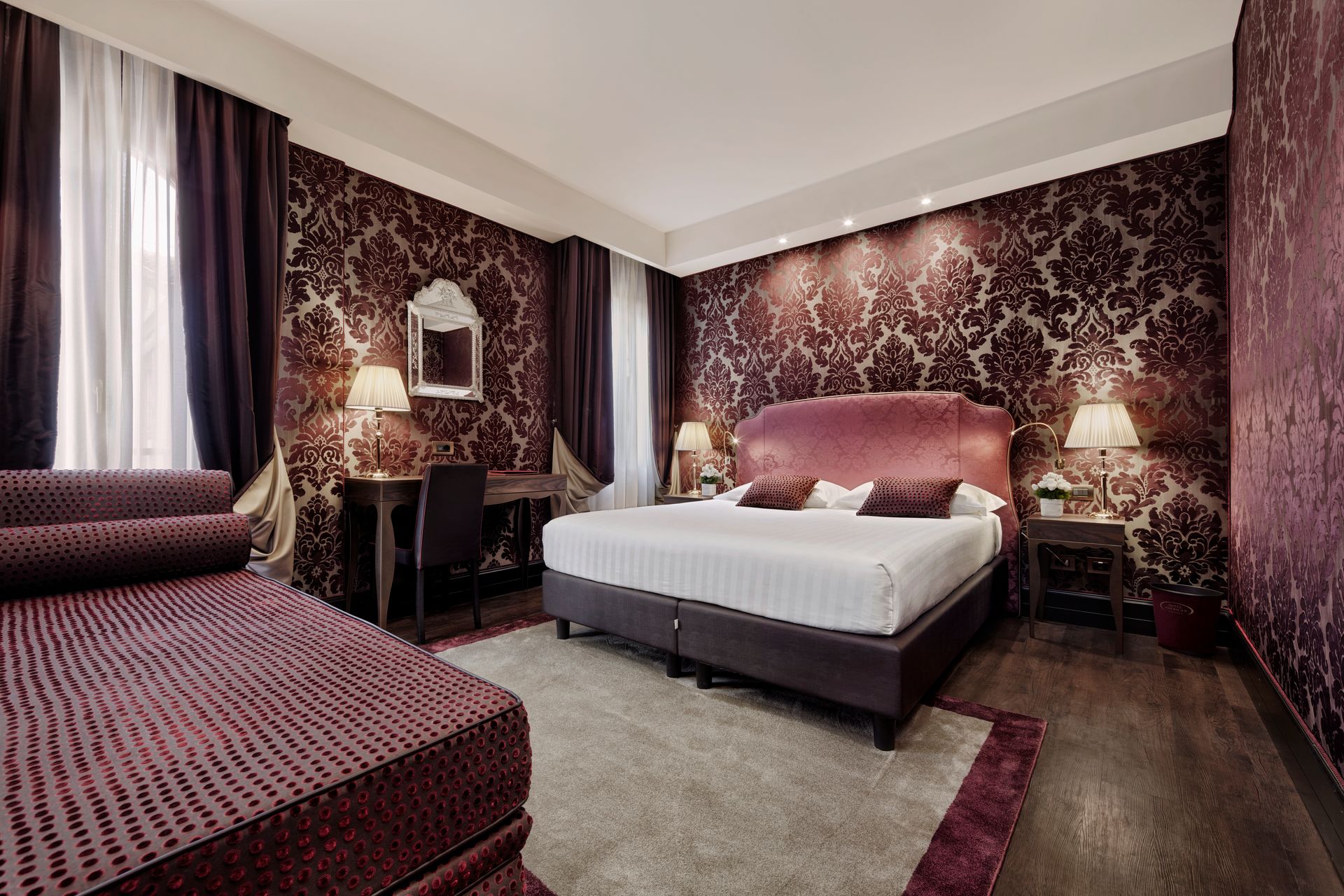 Elegante camera da letto con carta da parati a motivi bordeaux, letto rosa e chaise longue abbinata.