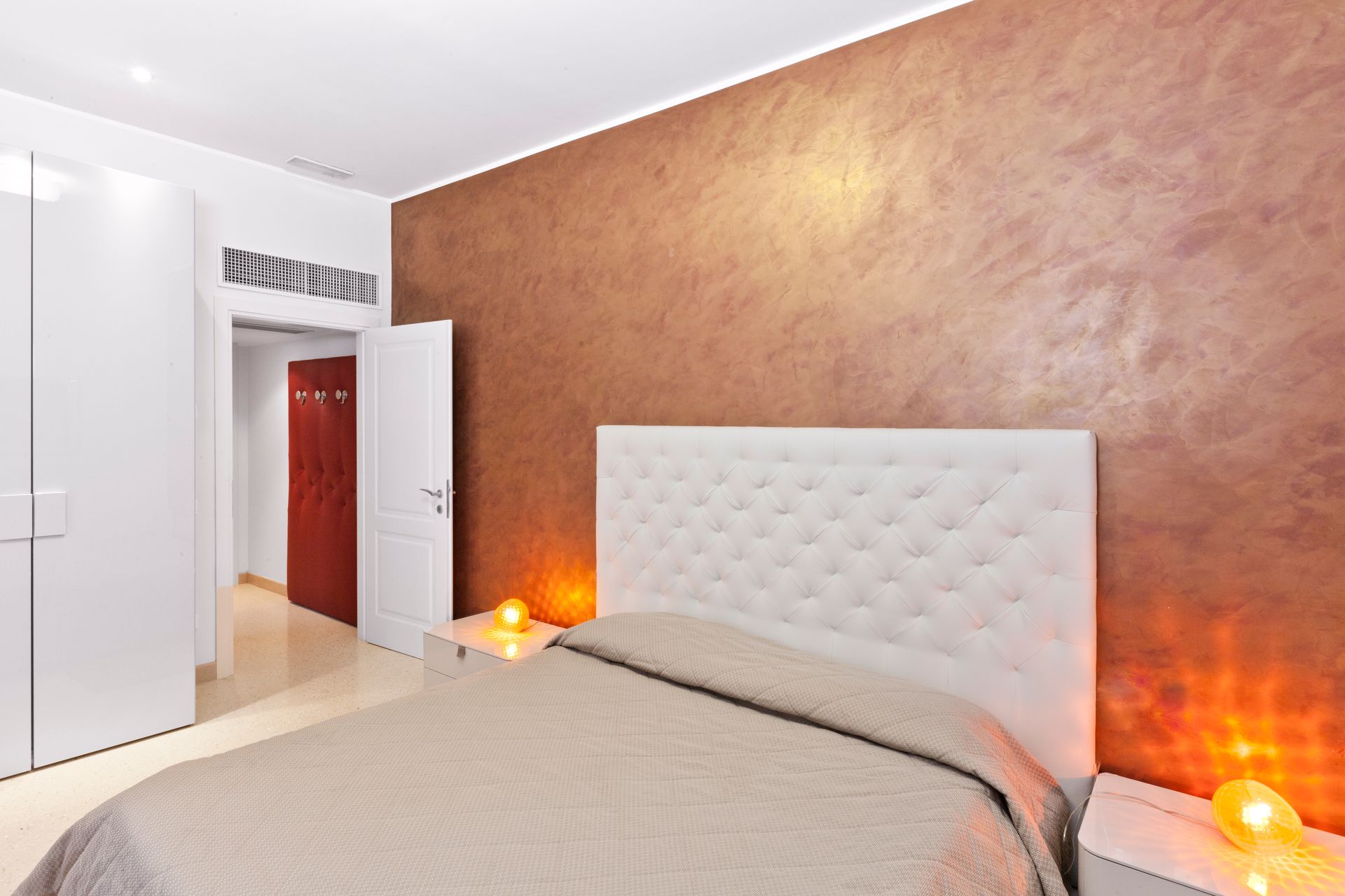 Camera da letto moderna con letto beige, testiera bianca trapuntata e parete decorativa