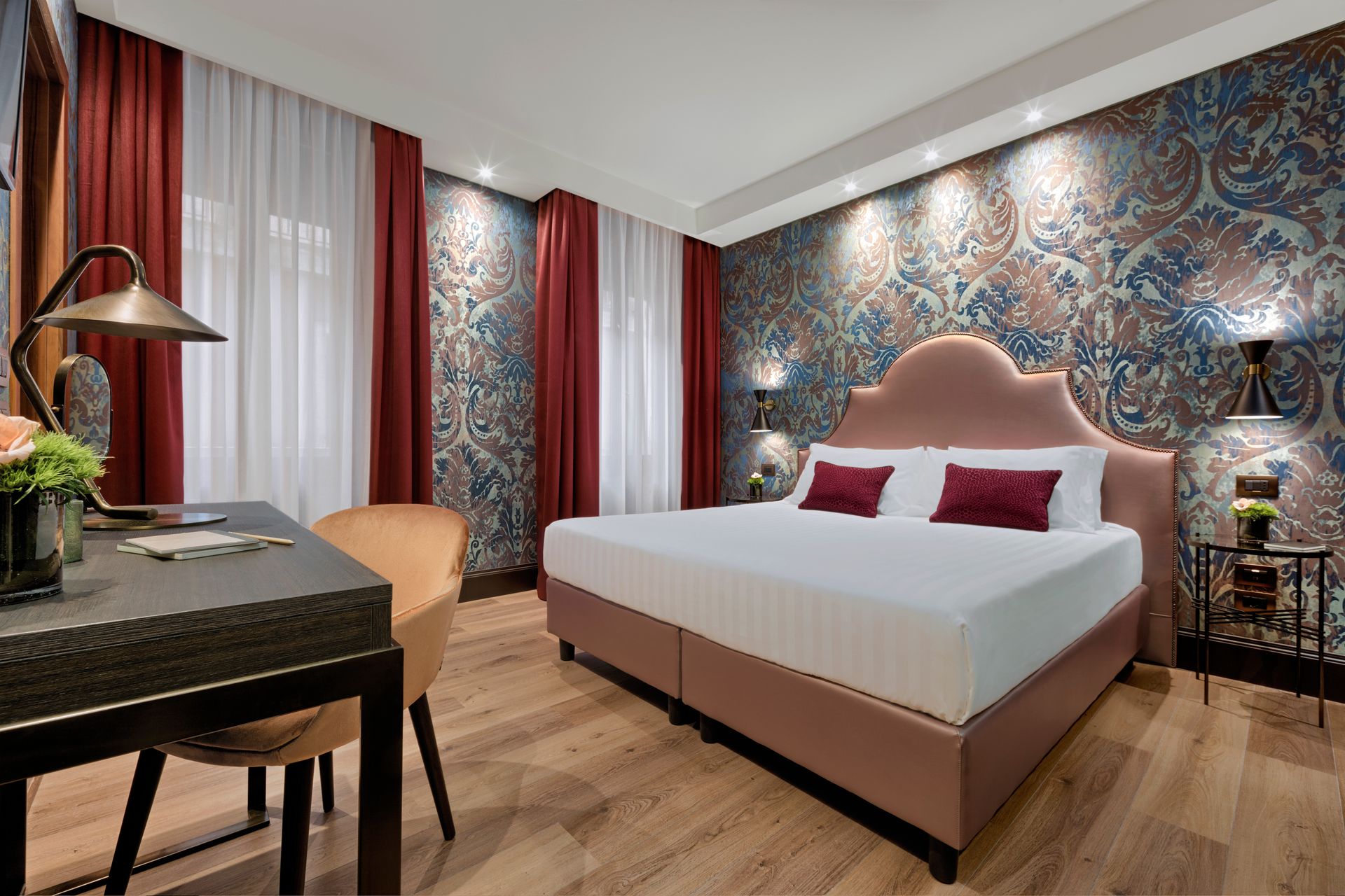 Camera da letto moderna con un grande letto, una parete decorativa con motivi geometrici, tende rosse e una scrivania