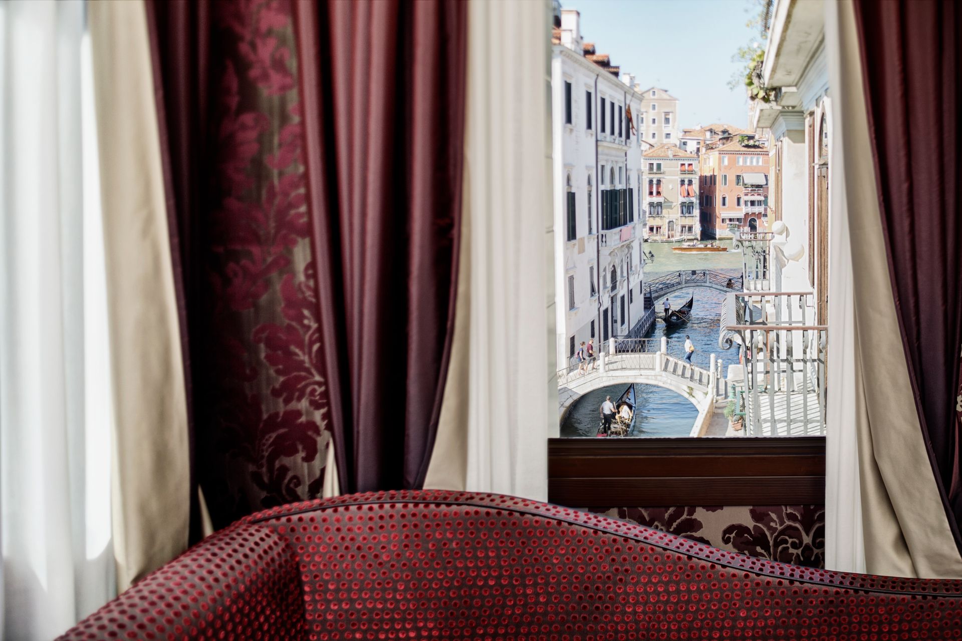 Divano in velluto rosso accanto a una finestra con tende color bordeaux che si affaccia su un canale