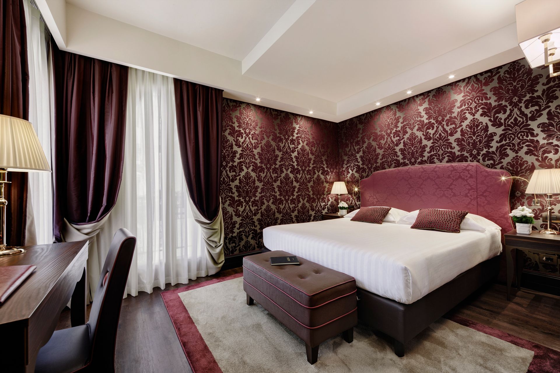 Elegante camera da letto con carta da parati a motivi bordeaux, letto grande, lampade da comodino e una finestra