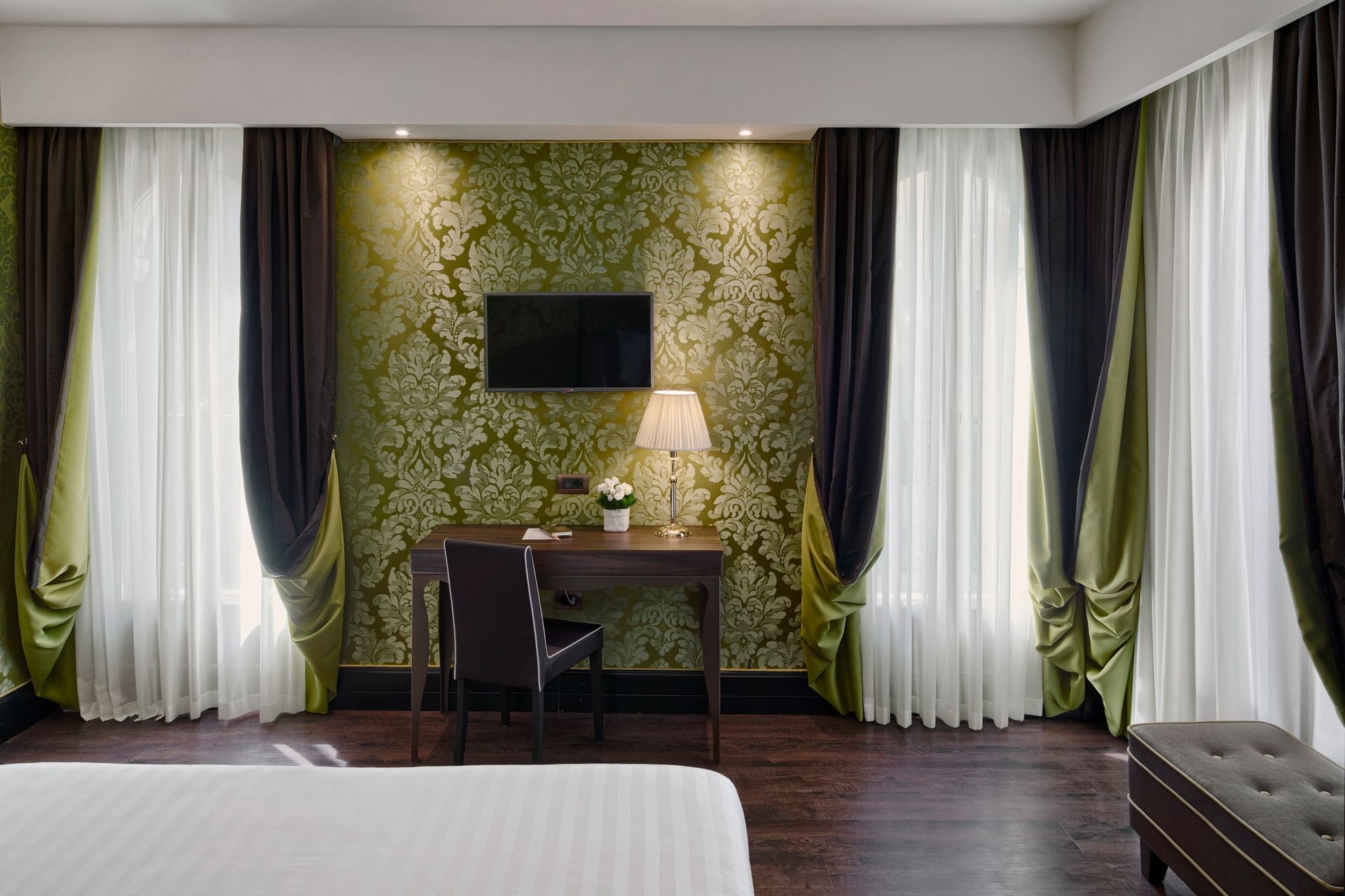 Camera d'albergo con scrivania, lampada, TV a parete e parete decorativa con motivo verde.