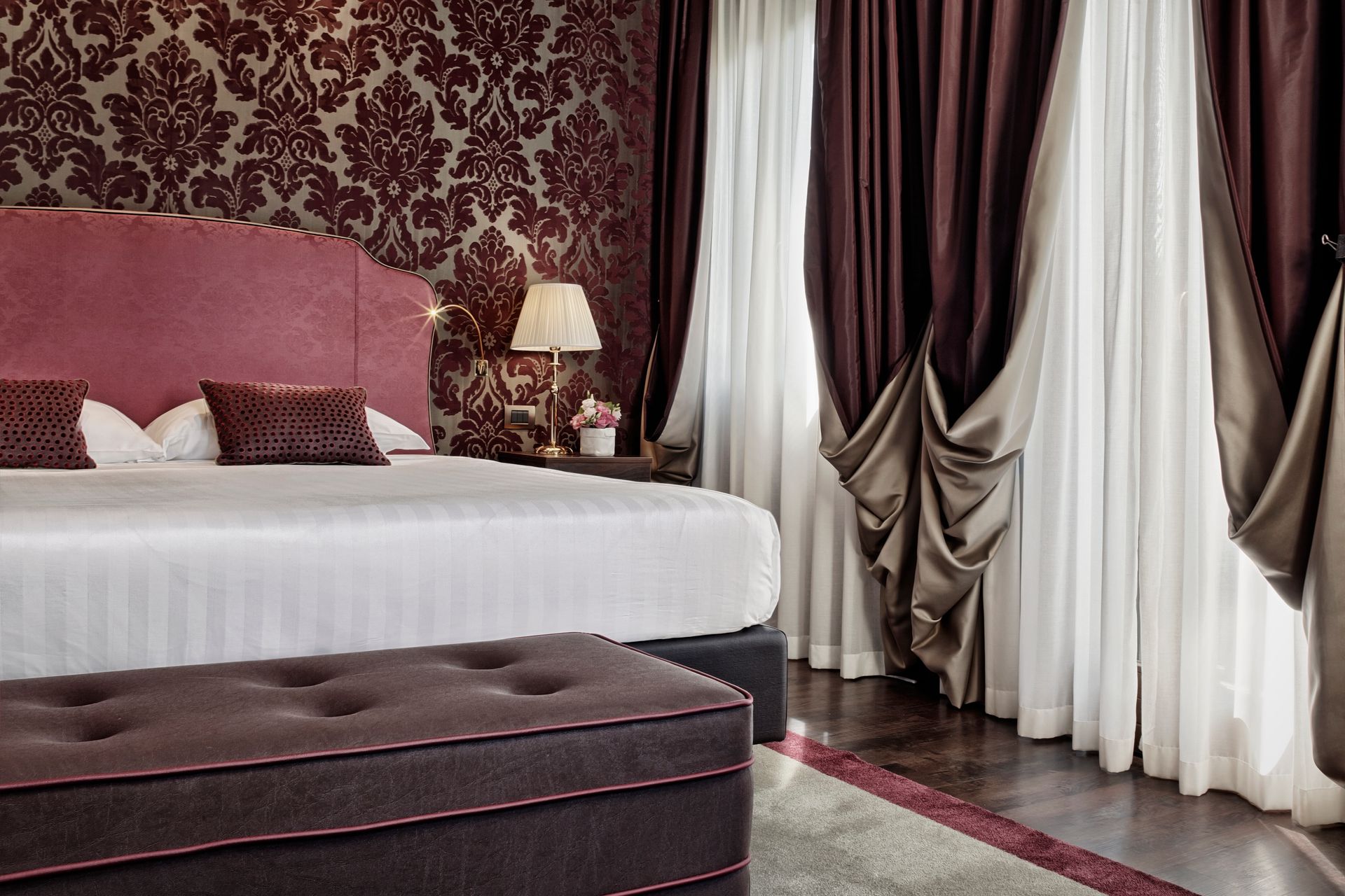 Elegante camera da letto con letto capitonné, carta da parati color bordeaux e tende drappeggiate.