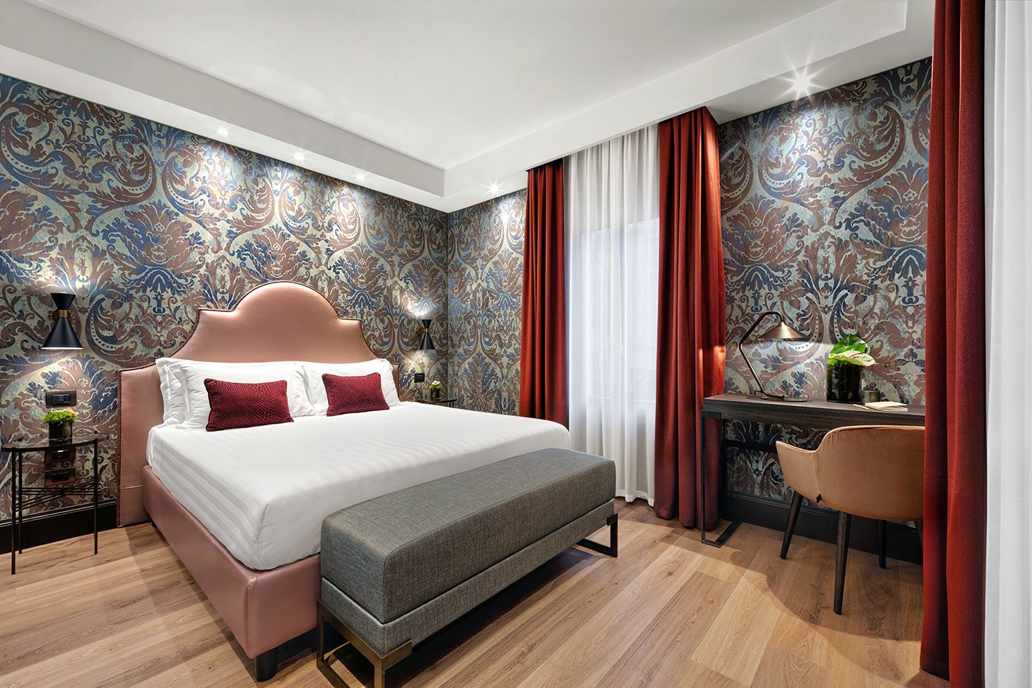 Camera da letto moderna con letto rosa, carta da parati a motivi geometrici, lampade da comodino e scrivania