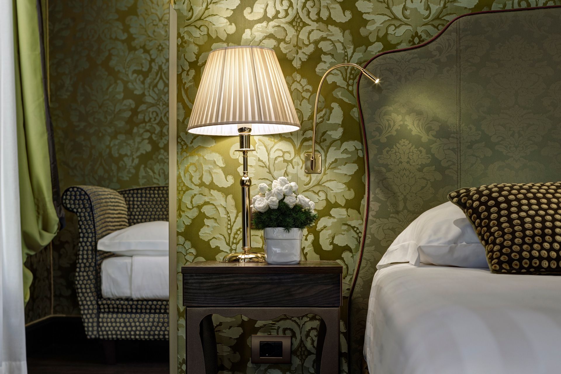Elegante camera da letto con due letti, una lampada da tavolo accesa e carta da parati a fiori verdi.