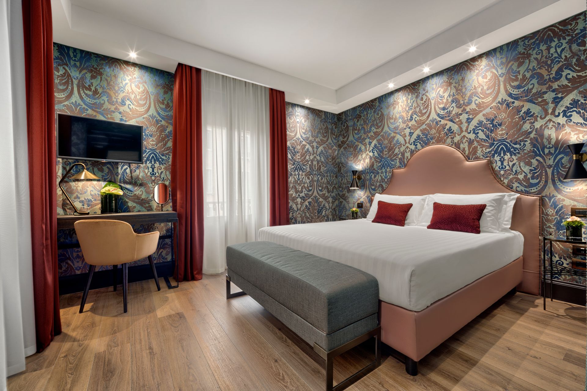 Elegante camera d'albergo con carta da parati a motivi, letto king size, scrivania e tende rosse.