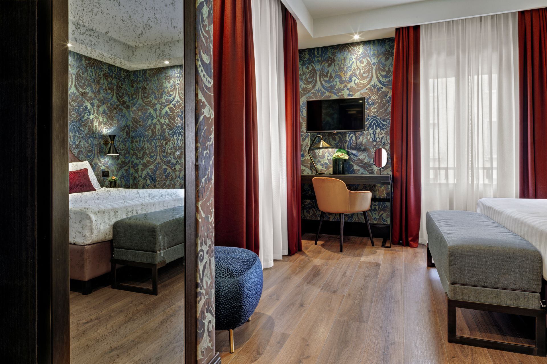Camera d'albergo moderna con due letti singoli, una scrivania vicino alla finestra e tende rosse che separano lo spazio