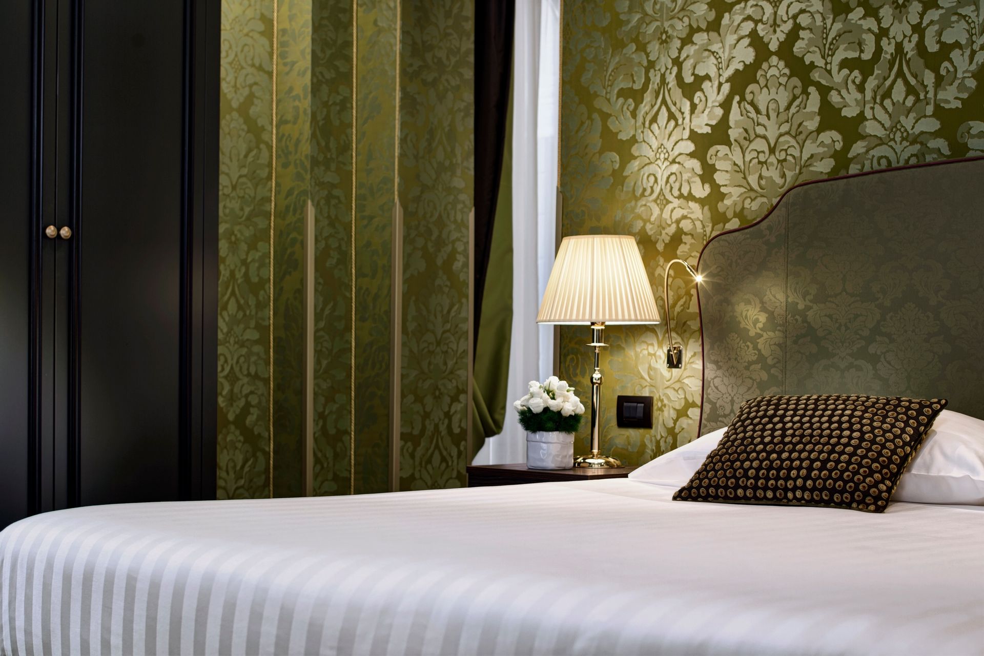 Elegante camera da letto con carta da parati verde, testiera imbottita, copriletto a righe bianche e lampada