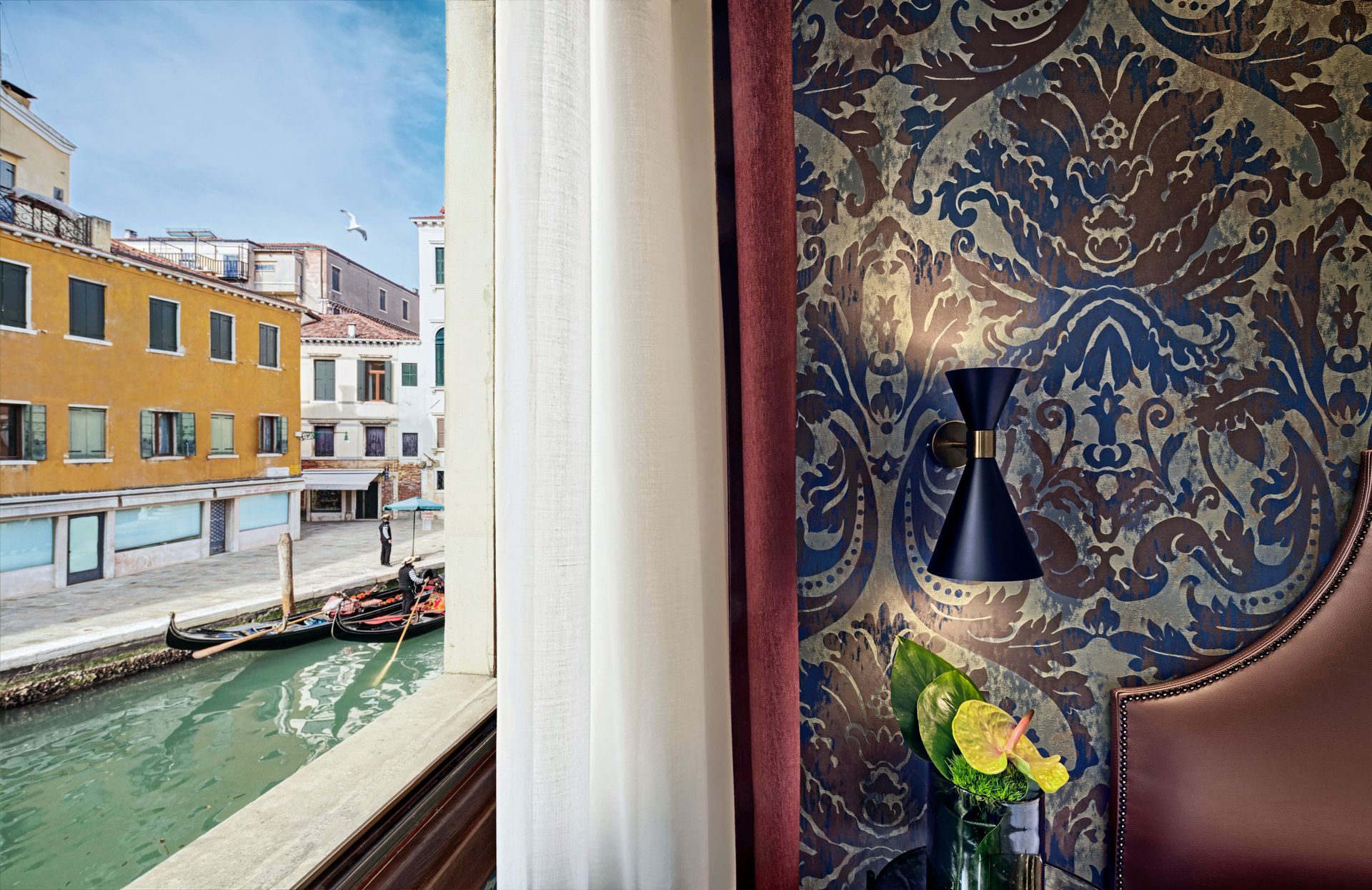 Vista sul canale attraverso una finestra accanto a una carta da parati blu a motivi geometrici e una lampada con fiori