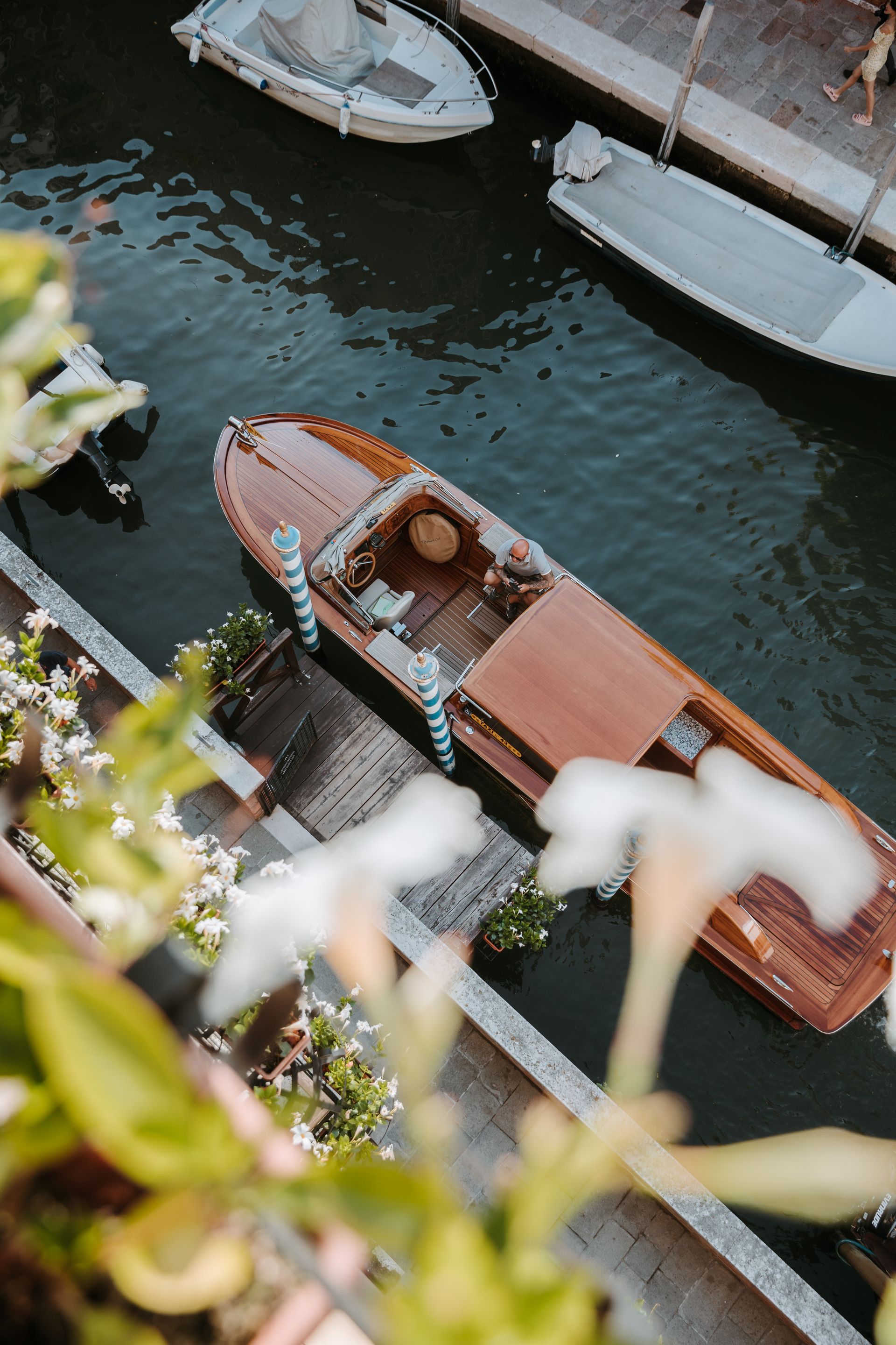 Deux bateaux bruns amarrés le long d'un canal, près d'un quai, vus du ciel, avec un feuillage flou au premier plan.