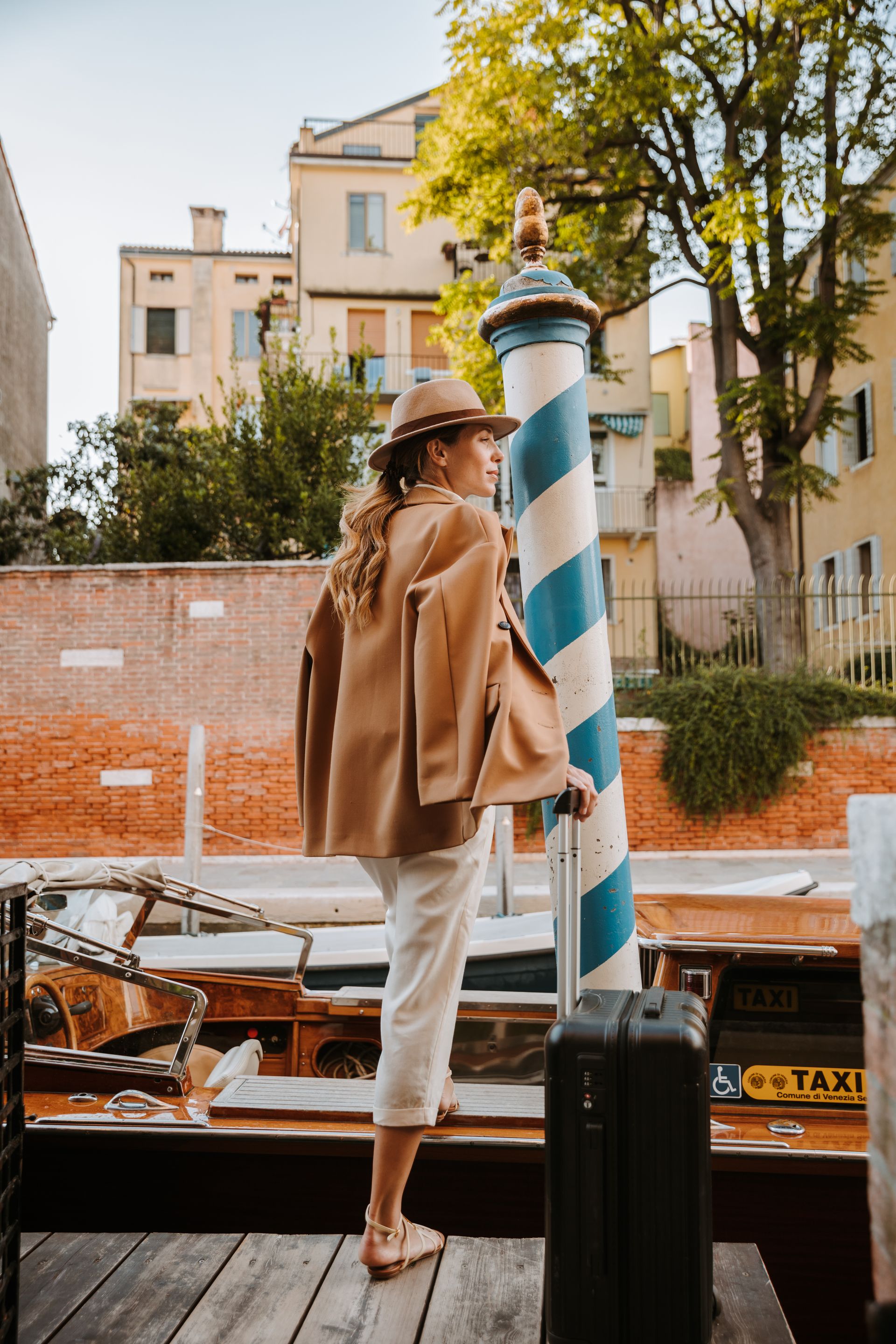 Une personne en manteau et chapeau beige se tient près d'un poteau de canal à rayures bleues et blanches, à côté d'un bateau