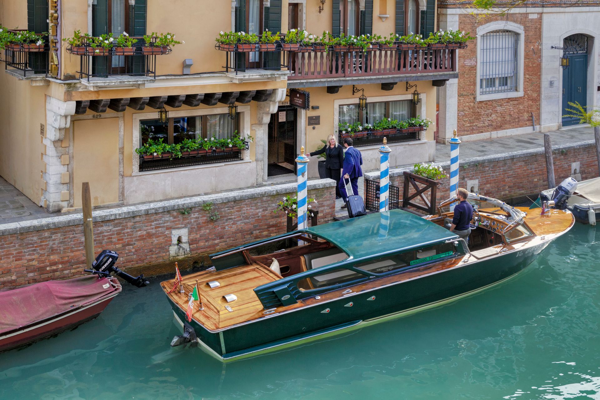 Una barca sul canale è attraccata accanto a un edificio veneziano adornato di fiori, con persone