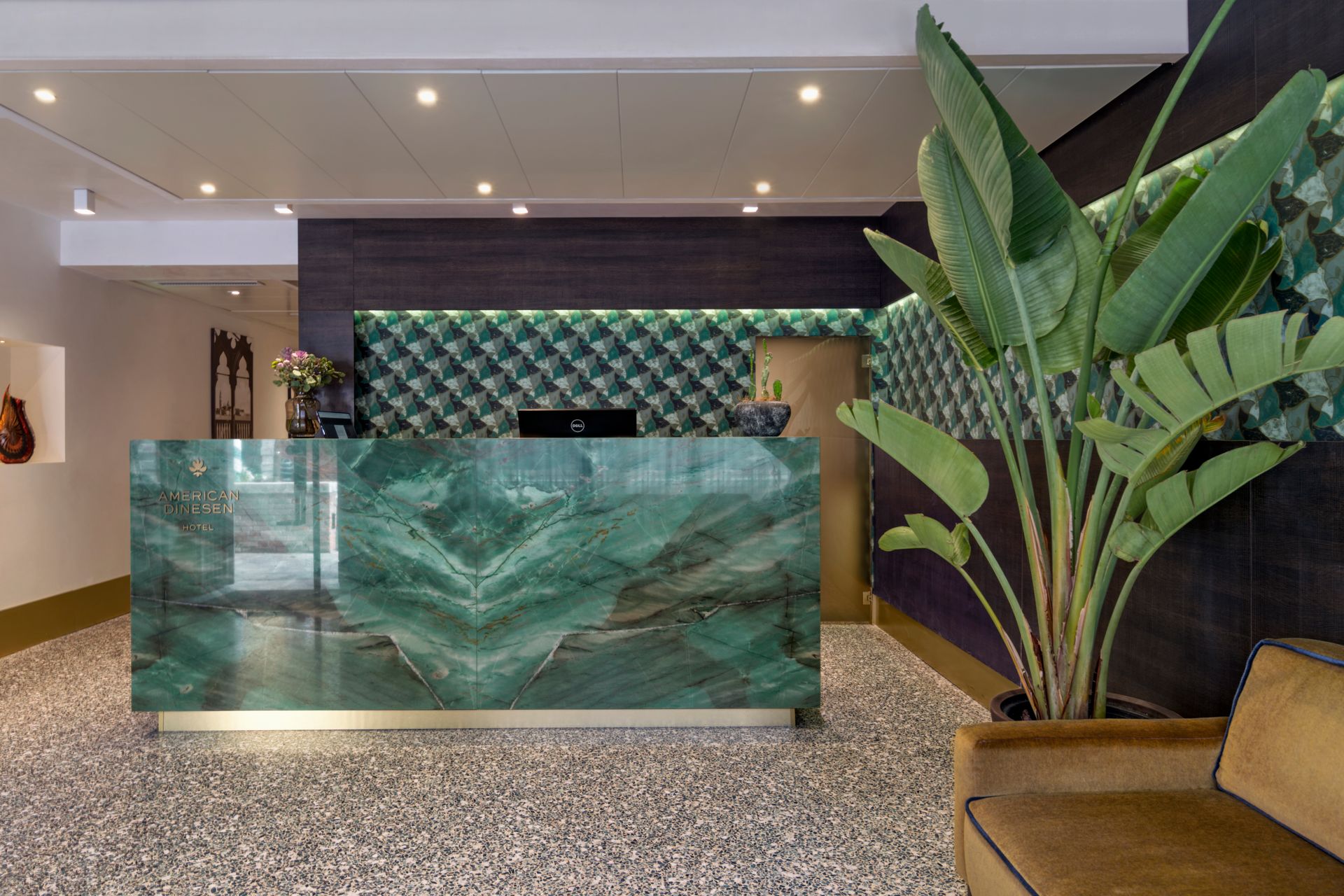 Modern hotel lobby with green marble reception desk, patterned wall, and large potted plant