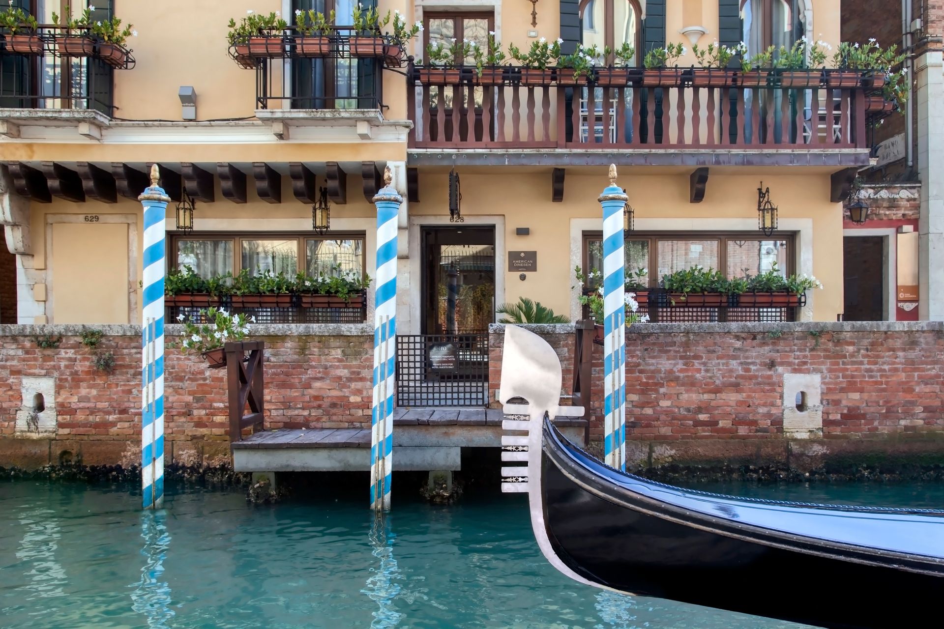 Venezianischer Kanal mit gestreiften Anlegepfählen, Gondelbug und einem mit Balkonen versehenen Gebäude über dem Wasser