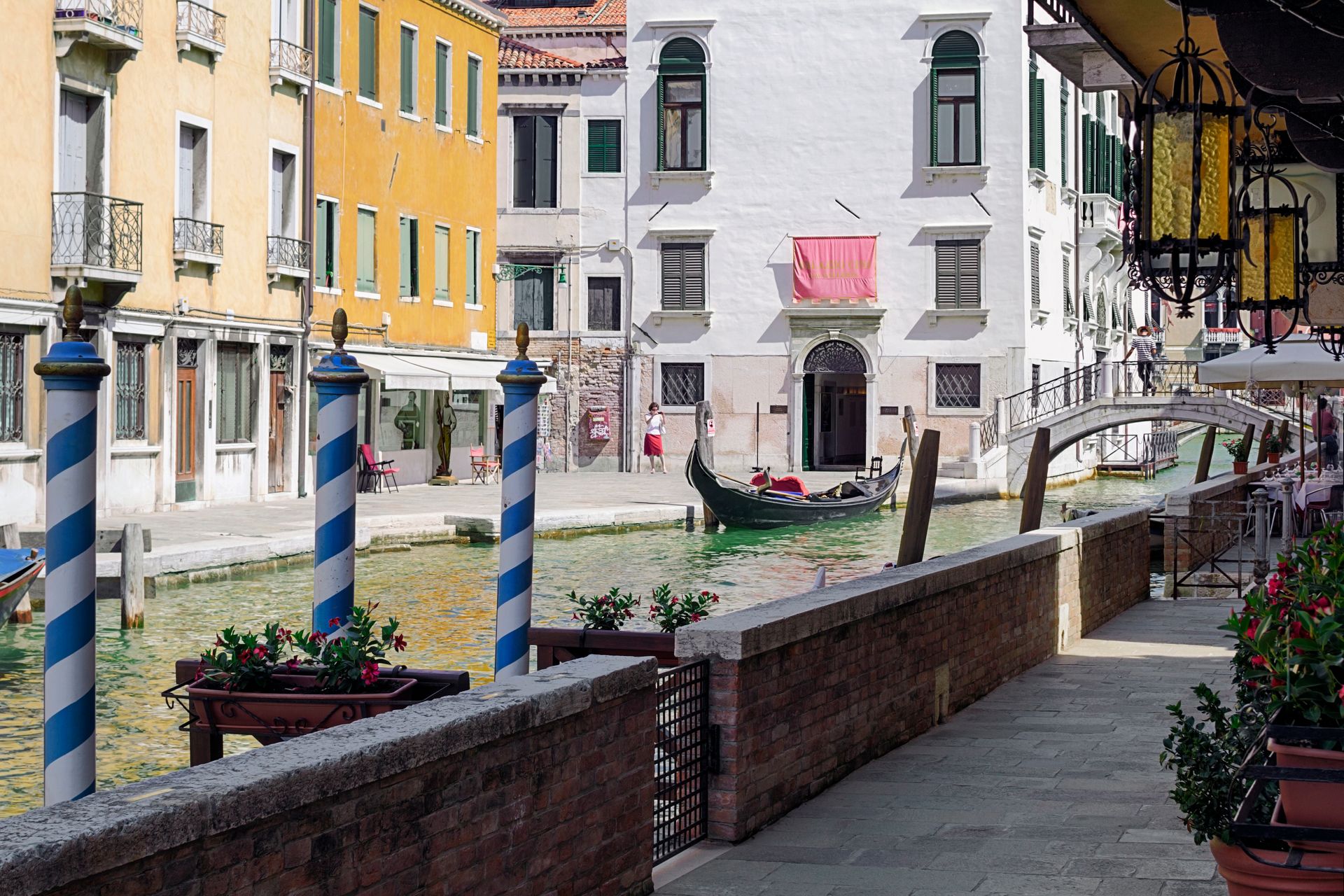 Passeggiata colorata lungo il canale con pali di ormeggio a strisce, muri in mattoni ed edifici lungo l'acqua.