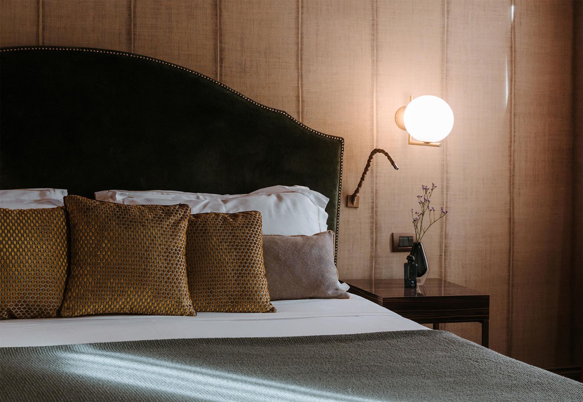 Chambre confortable avec une tête de lit vert foncé, des coussins texturés et une lampe de chevet allumée