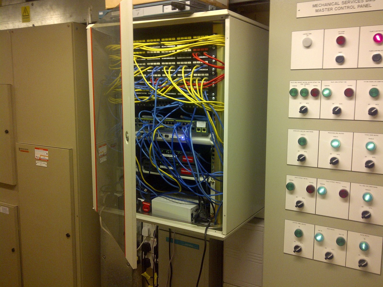 Network server cabinet with tangled wires; control panel with illuminated buttons.