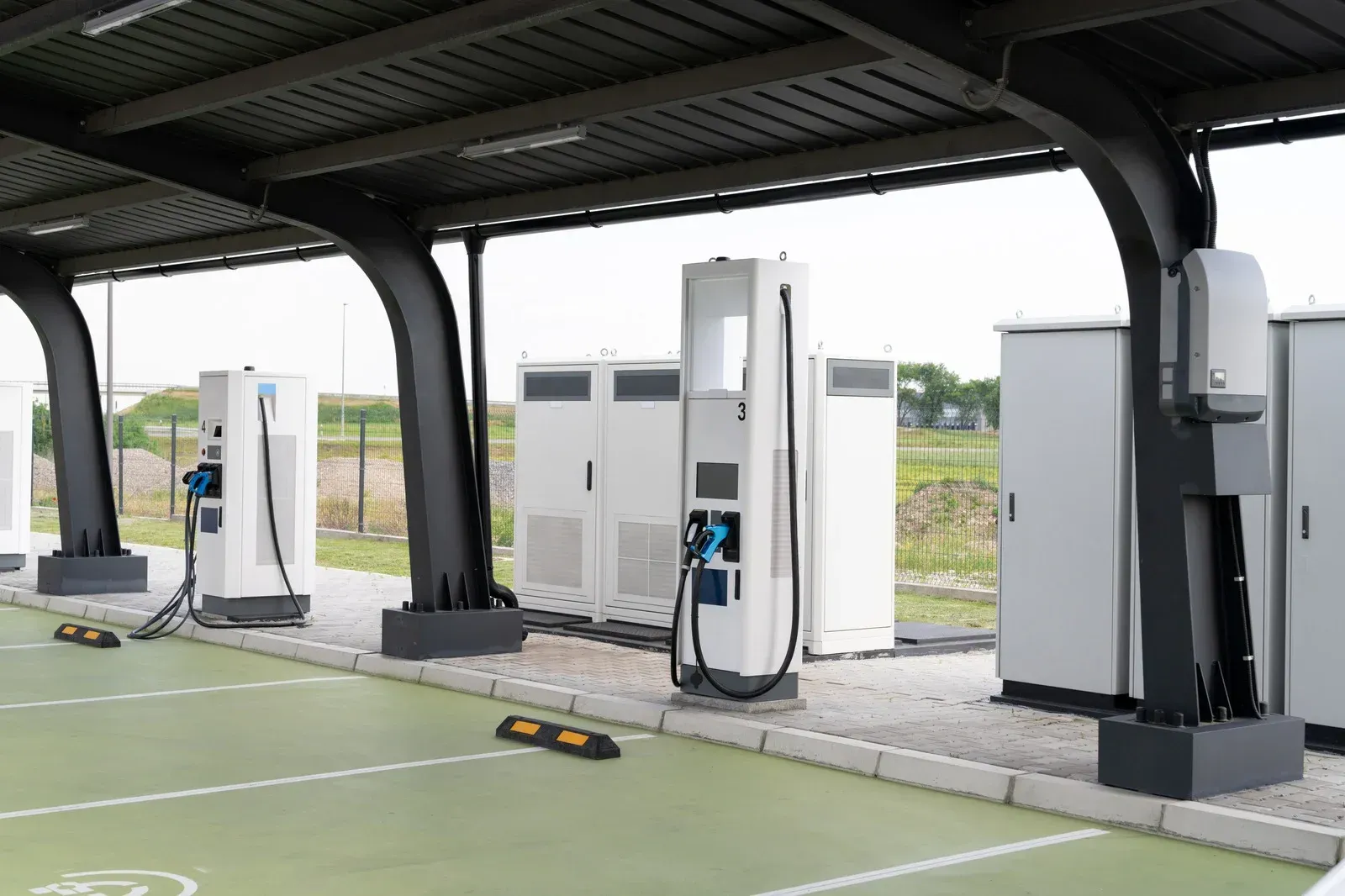 Electric vehicle charging station with multiple white chargers under a black canopy.